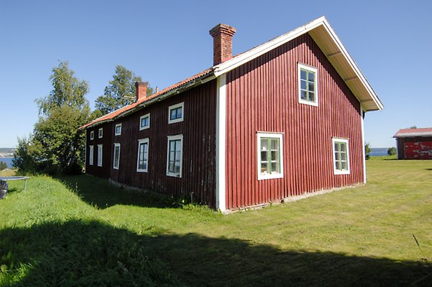 Namn 2:18. Byggnad i röd panel med vita detaljer, i två våningar, fönster med gröna spröjs, två skorstenar i tegel.