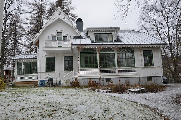 Frösö 437. Villa i vit panel med gröna fönster med spröjs, veranda med snickarglädje. 