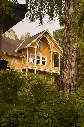 Lantmätaren 10. Villa med gul panel och balkong med snickarglädje.