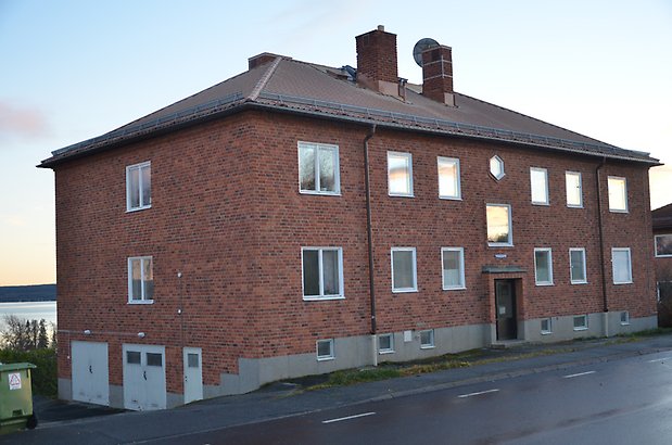 Majoren 2. Bostadshus i tre våningar i brunt tegel med vita fönster och grå garageportar på kortsidan.