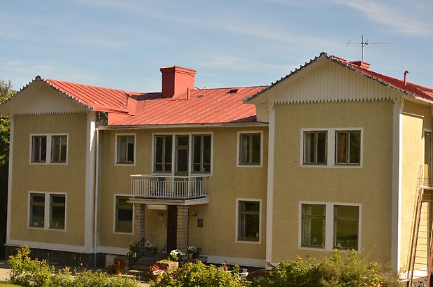 Östbergsgården 1. Bostadshus i gul puts med vita detaljer och gröna fönster, vit balkong och rött plåttak. 