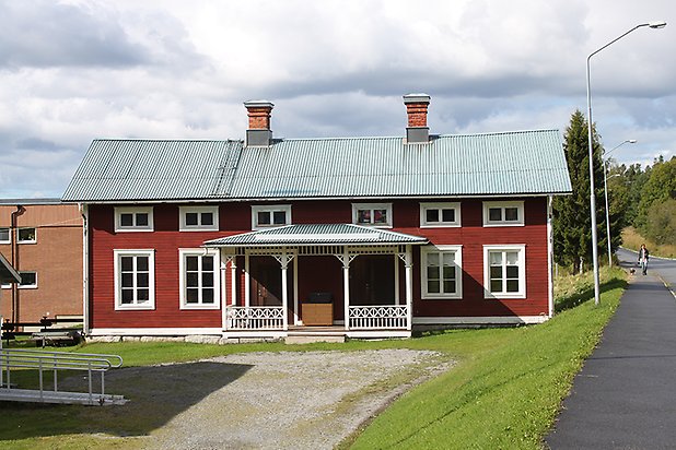 Villa i röd liggande panel, vita fönster med spröjs, förstukvist med snickarglädje.