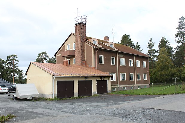 Flerbostadshus i två våningar i brun puts med beige detaljer. Vita fönster och tegeltak med takkupa.