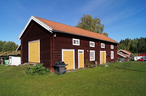 Torvalla 4:50. Brun timrad ladugård, fönster med vita spröjs, gula dubbeldportar.