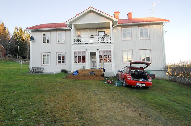 Lockne-Berge 2:2. Villa i vit panel med röda detaljer i två våningar, punschveranda med balkong ovanför med vit snickarglädje, fönster med vita spröjs. 