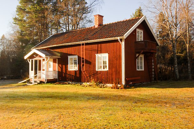 Lockne Prästbord 1:2. Hus i röd panel i två våningar, förstukvist i vitt och rött, balkong i rött på kortsidan, fönster med vita spröjs och murad skorsten.