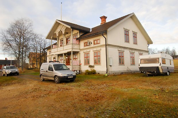 Ångsta 2:2. Villa i två våningar, i ljus, liggande panel med grå och röda detaljer, förstukvist och balkong med snickarglädje.