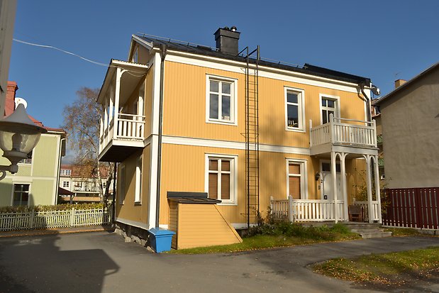 Trähus i två våningar i gul panel, vita knutar, fönsterfoder och detaljer. Vita fönster med spröjs.