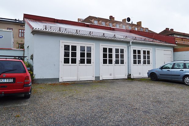 Byggnad i ljusblå puts med tre vita garageportar med fönster och en garageport utan. Rött plåttak.