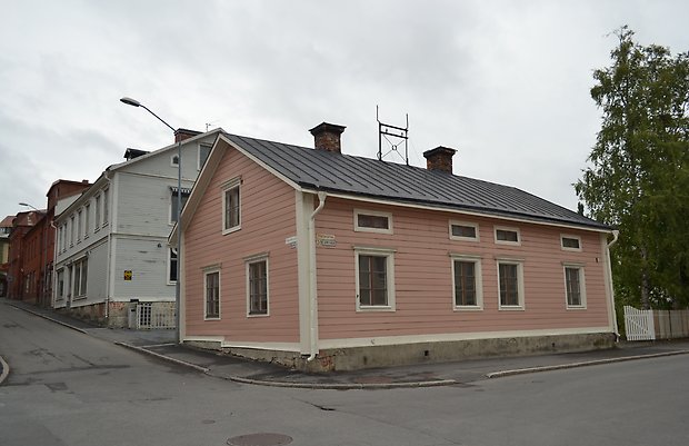 Tvåvåningshus i rosa liggande träpanel med vita knutar och vita fönster med bruna spröjs och svart plåttak.