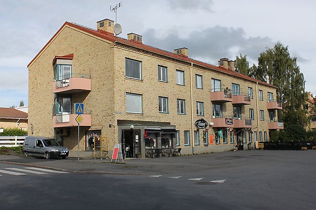 Bergsvik 9. Flerbostadshus i gult tegel i tre våningar med rosa balkonger och butikslokal på nedervåningen. 