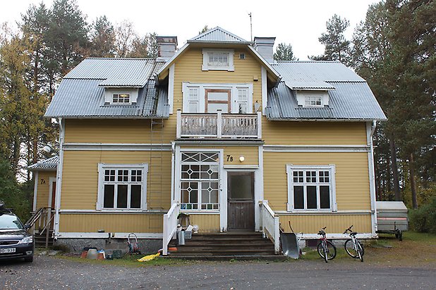 Söre 5:27. Villa i gul, liggande panel med vita fönster med spröjs och lite punschveranda med balkong.