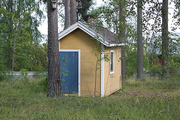 Söre 2:14. Litet hus i gul, liggande panel med vitt fönster och blå dörr.