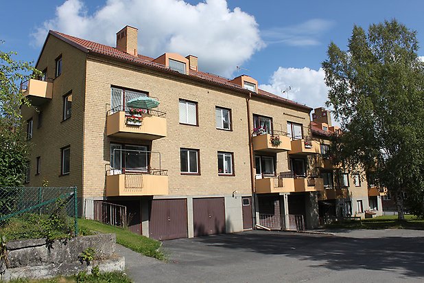 Söre 2:98. Flerbostadshus i fyra våningar i gult tegel med gula balkonger, bottenvåningen har bruna garagedörrar.