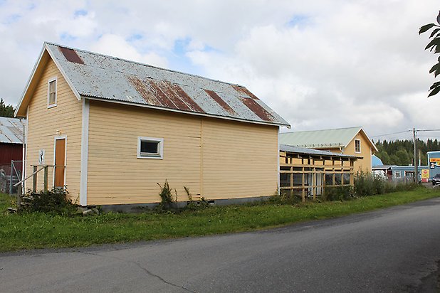 Söre 3:57. Byggnader i gul, liggande panel, brun dörr och små fönster.