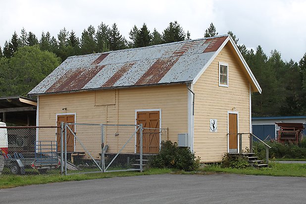 Söre 3:57. Byggnad i gul, liggande panel, brun dörr och små fönster.