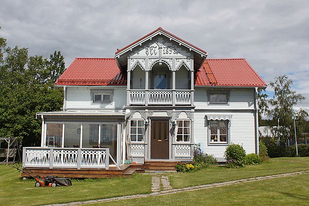 Orrviken 5:1. Villa i vit liggande panel med grå fönster med vita spröjs. Punschveranda och balkong med grå snickarglädje. Rött tak.