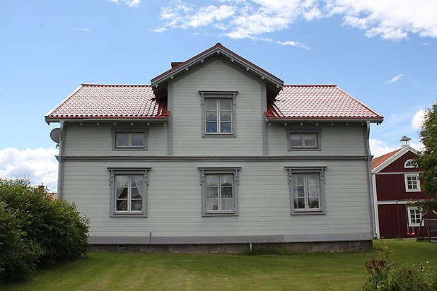 Orrviken 5:1. Villa i vit liggande panel med grå fönster med vita spröjs. Rött tak..