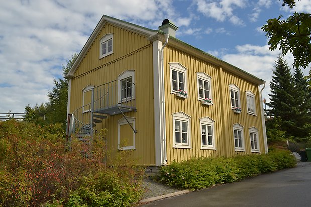 Trähus i tre våningar i gul panel. Vita detaljer, vita fönster med spröjs.