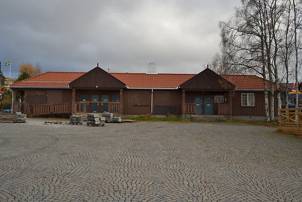 Träbyggnad i en våning i brun panel. Tegeltak. Blå portar, två förstukvistar med tak.