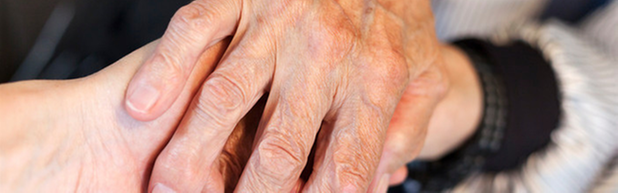 Detaljbild som föreställer en gammal människas hand som håller en ung människas hand.