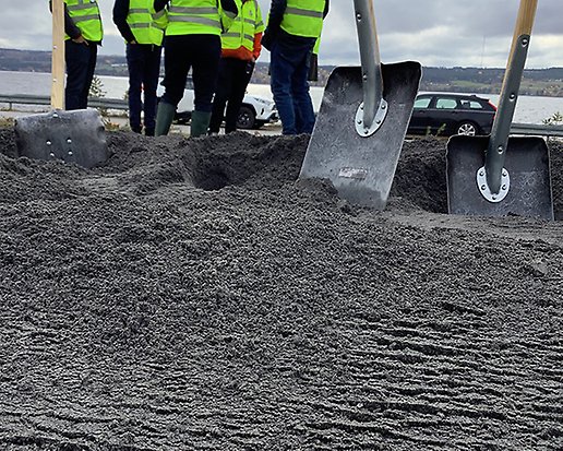 Spadar står i en grushög. I bakgrunden står ett antal människor i signalklädsel.